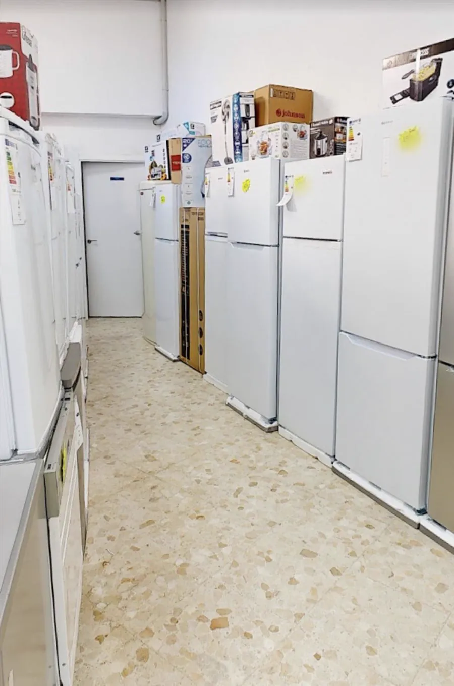 Pasillo de frigoríficos blancos en exposición, con pequeños electrodomésticos encima