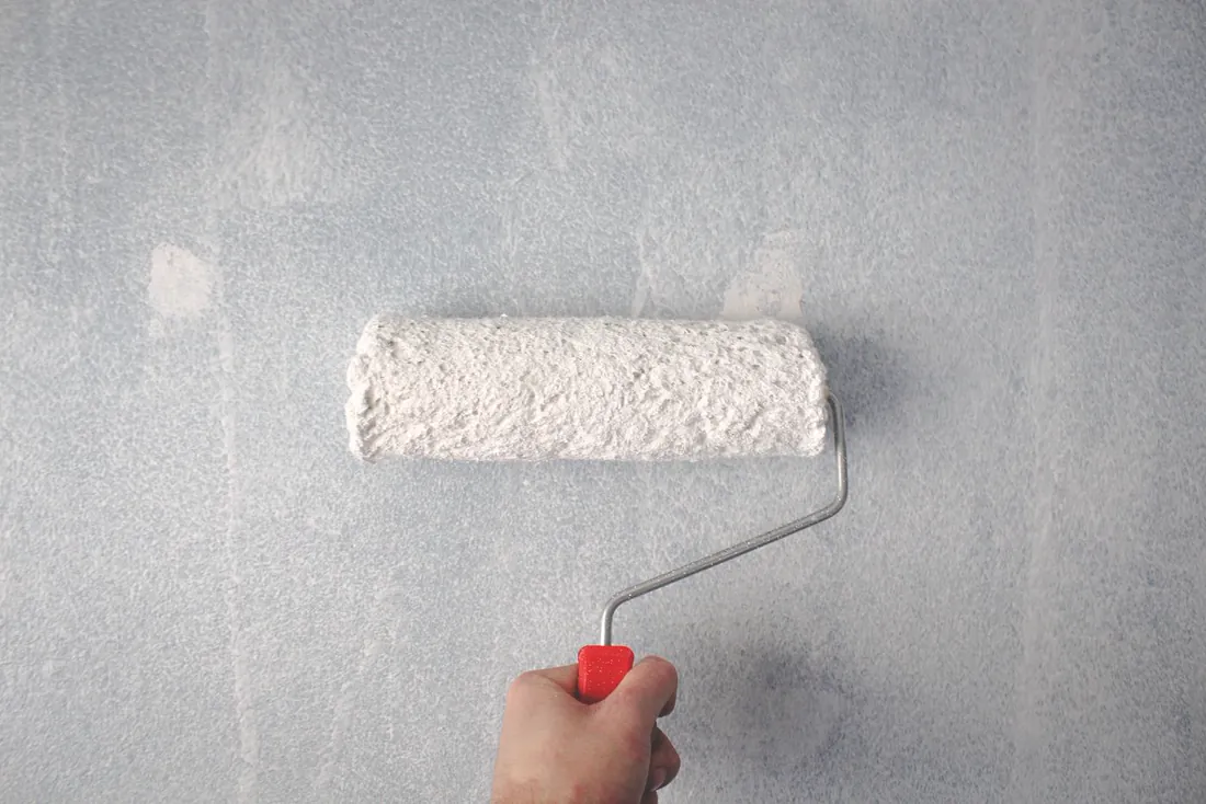 Mano pintando una pared con un rodillo de pintura blanca