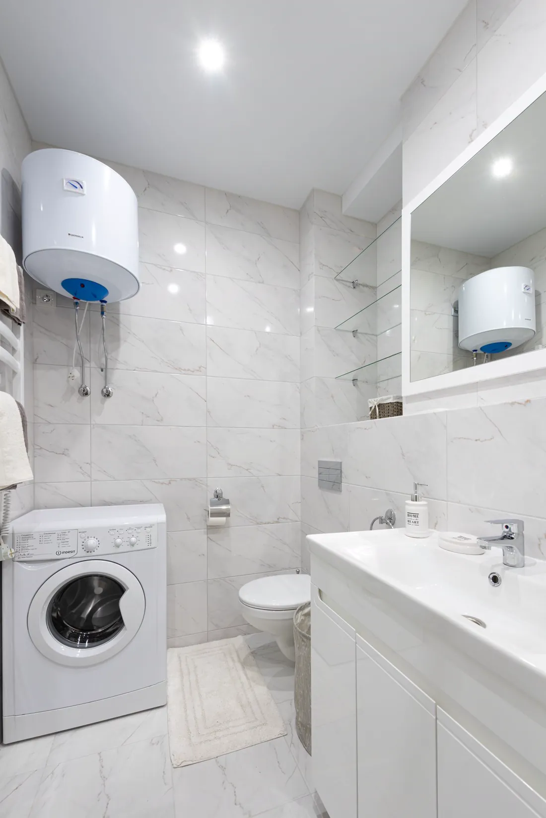 Termo eléctrico blanco instalado en la pared de un baño, sobre una lavadora
